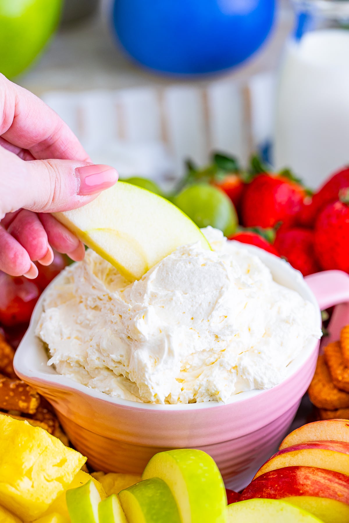 a hand dipping an apple slice into Cream Cheese Fruit Dip