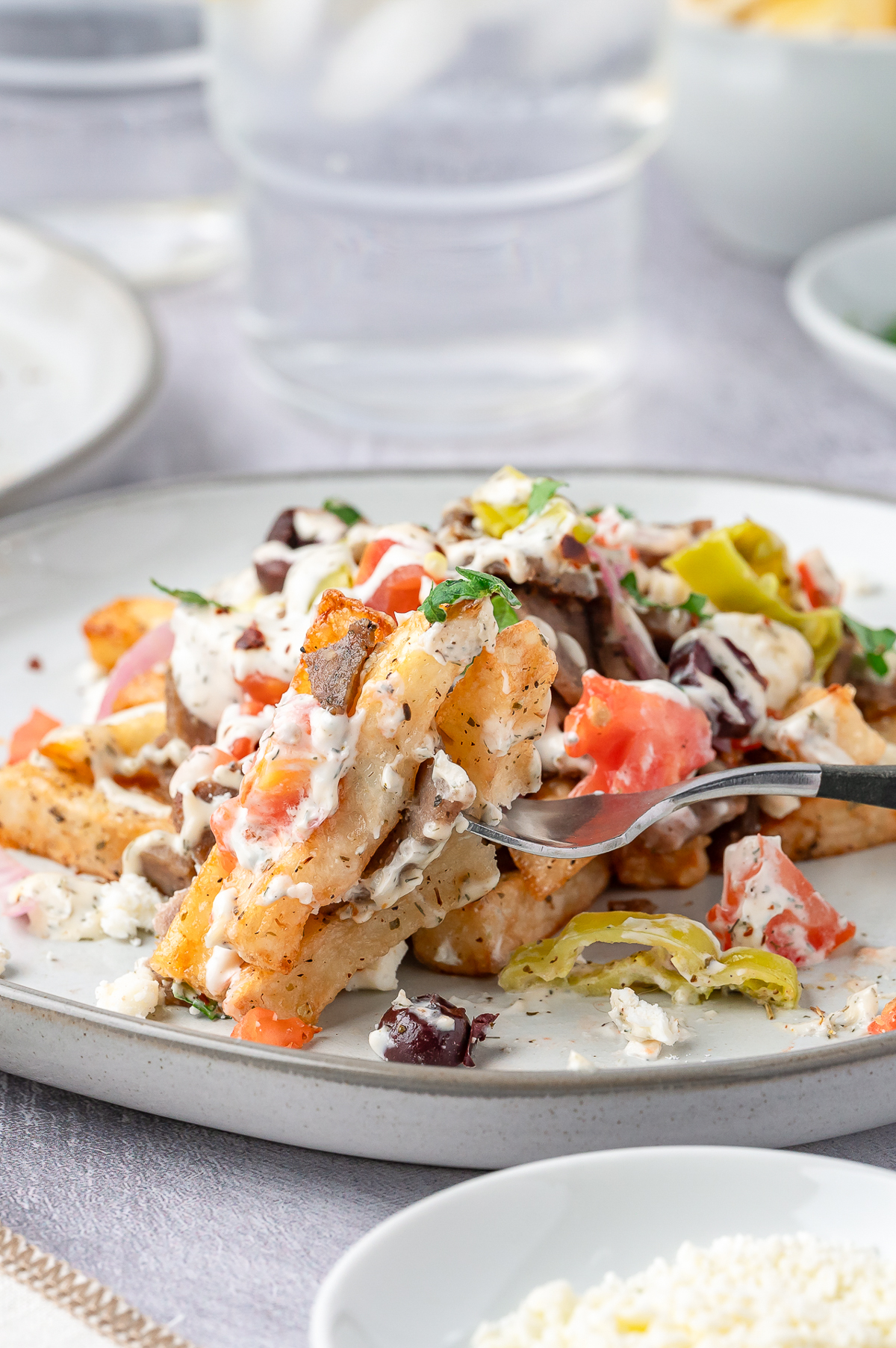 a fork grabbing a bite of Greek Fries on a plate
