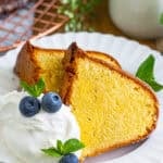 A slice of classic moist pound cake on a plate with whipped cream and blueberries
