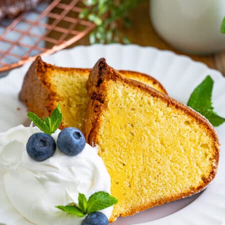 A slice of classic moist pound cake on a plate with whipped cream and blueberries