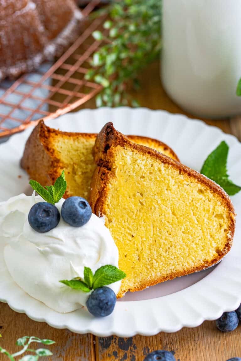 A slice of classic moist pound cake on a plate with whipped cream and blueberries