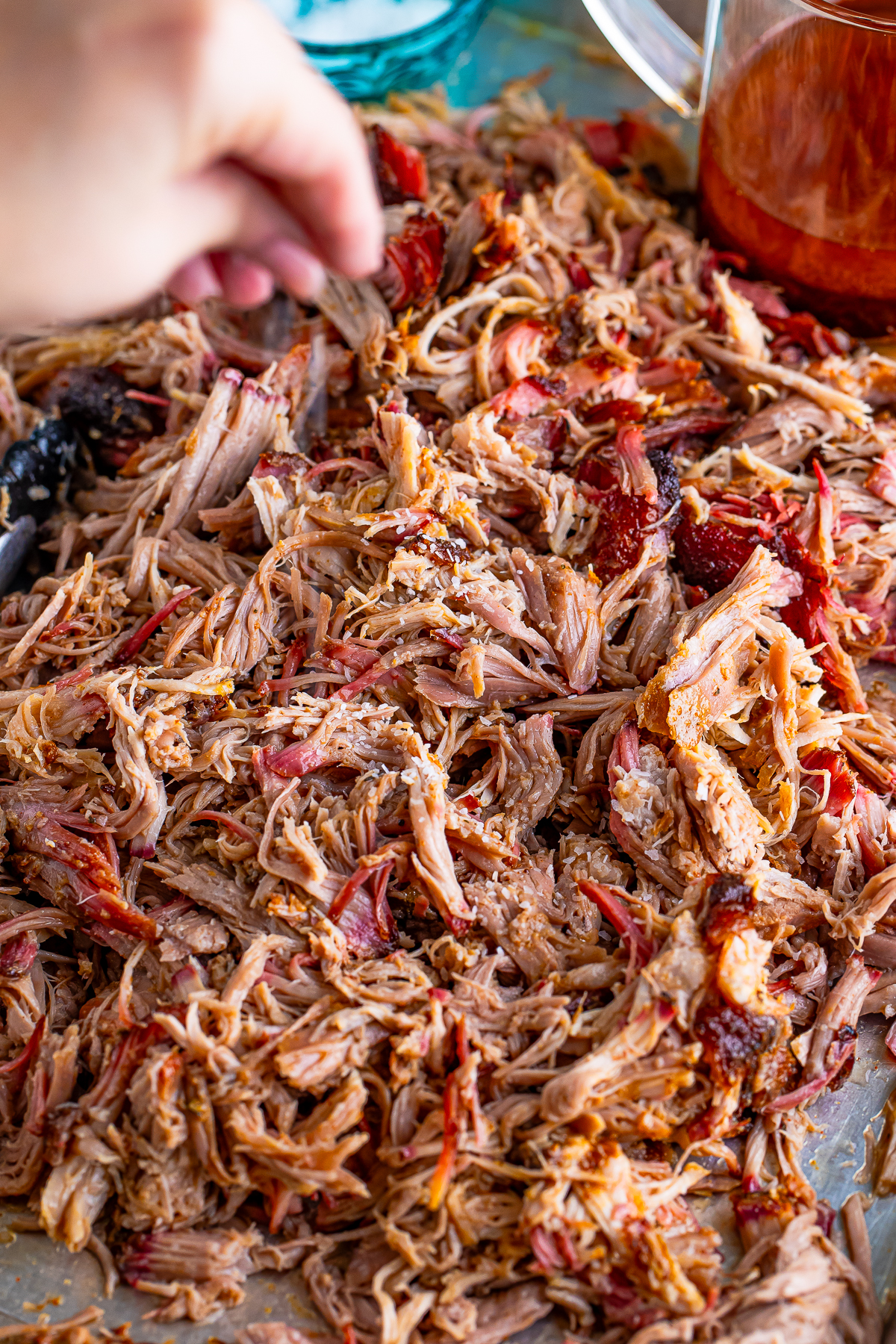 a hand sprinkling salt on Pulled Pork