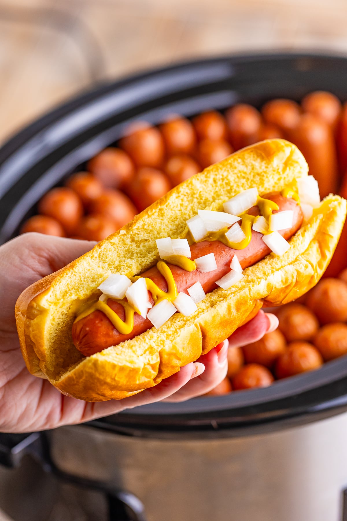 a hand holding up Slow Cooker Hot Dogs over the cooker