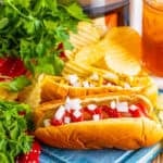 Easy Crockpot Hot Dogs Recipe served on a fluffy bun with toppings in front of a black slow cooker filled with cooked hot dogs.