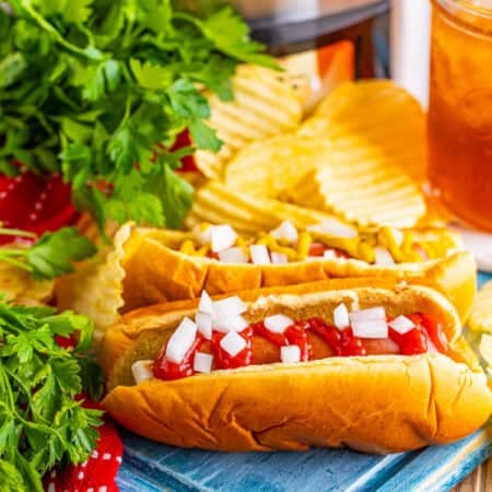 Easy Crockpot Hot Dogs Recipe served on a fluffy bun with toppings in front of a black slow cooker filled with cooked hot dogs.