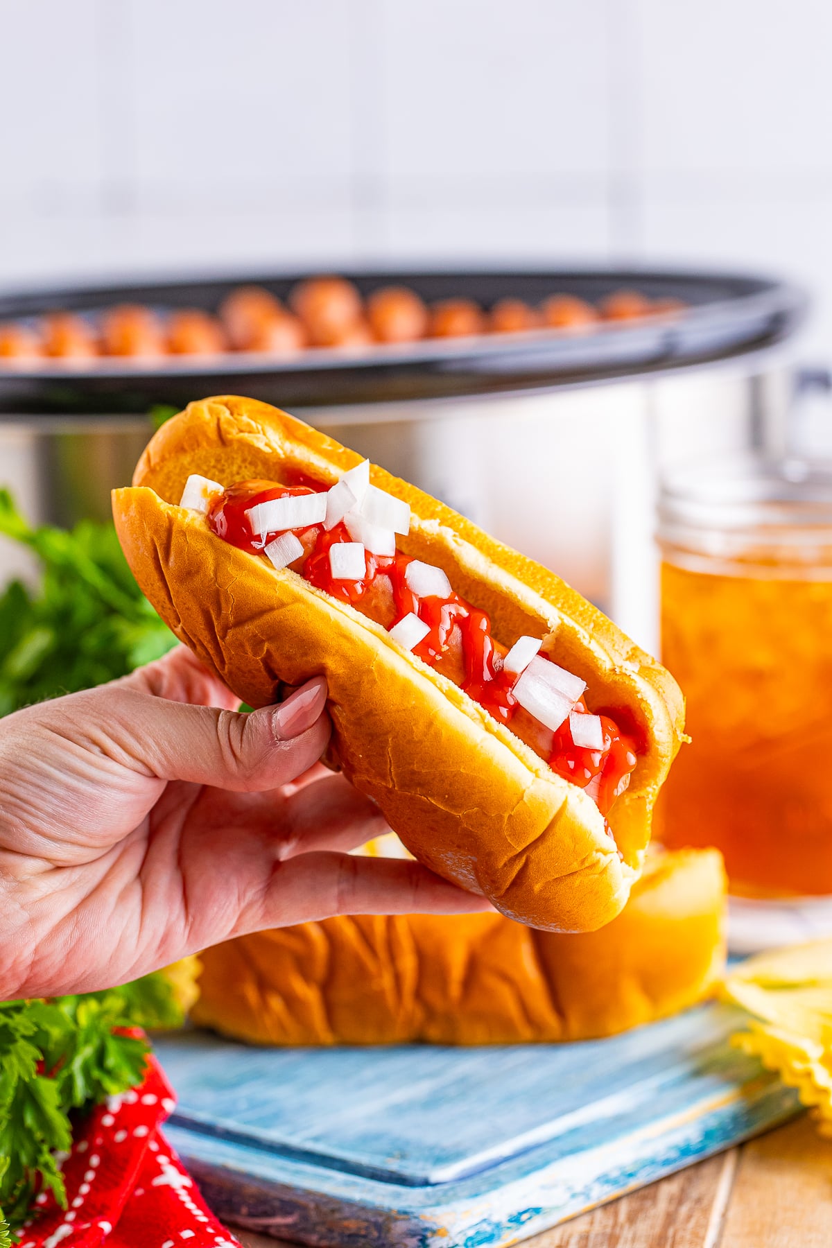 a hand holding up Slow Cooker Hot Dogs in the air