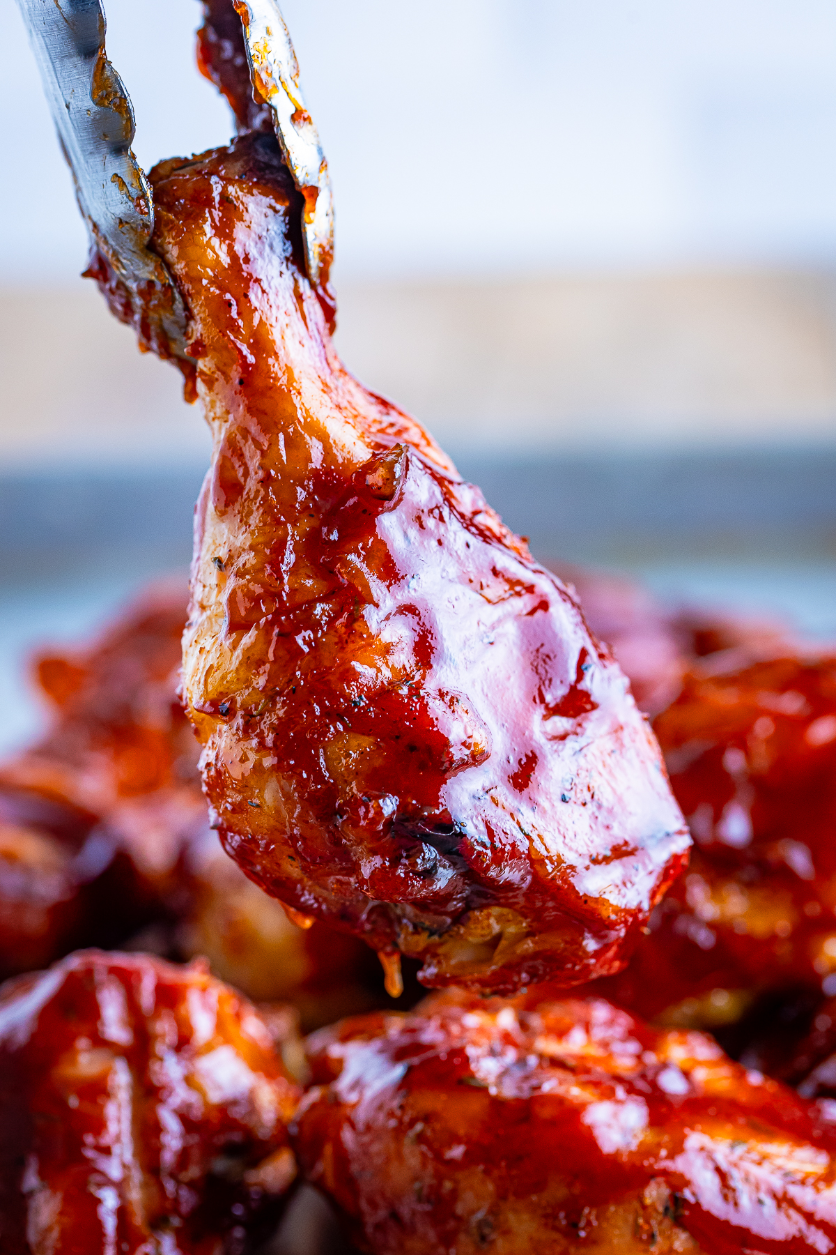 a pair of tongs holding up Smoked Chicken Legs in air