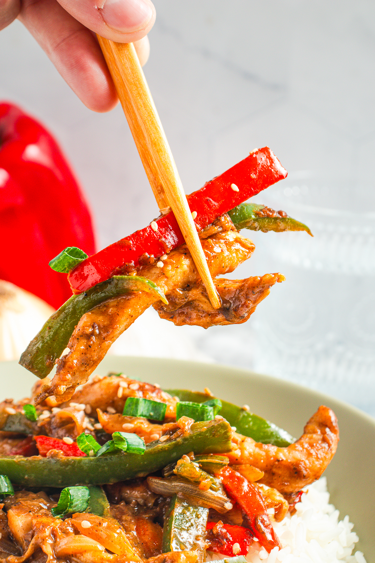 chopsticks holding up a bite of Black Pepper Chicken in air