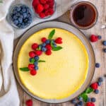 A whole cottage cheese cake topped with fresh berries on a dark plate.
