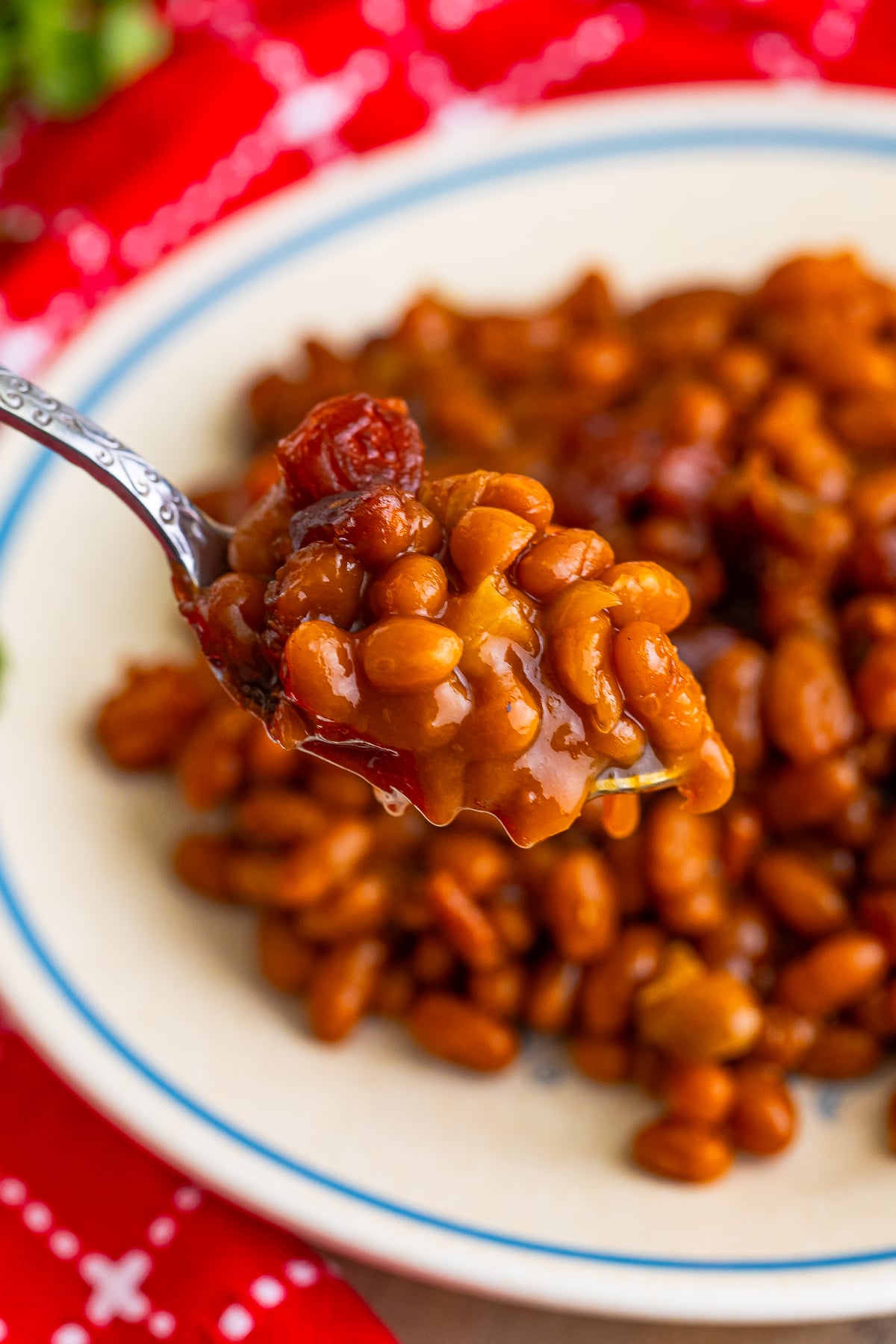 a small spoon holding up a bite of baked beans recipe in the air