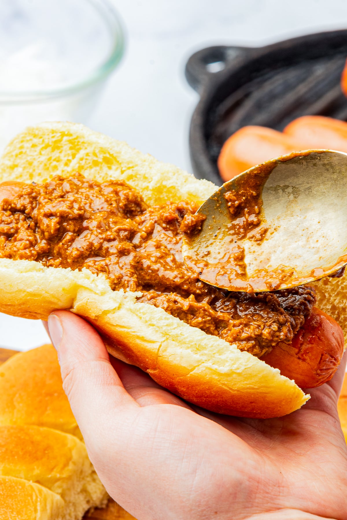 a spoon smearing Hot Dog Sauce on a hot dog