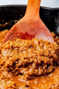 Close up of Coney Sauce Recipe on a spoon over the simmering pan, showing the fine-textured beefy sauce ready to top hot dogs.