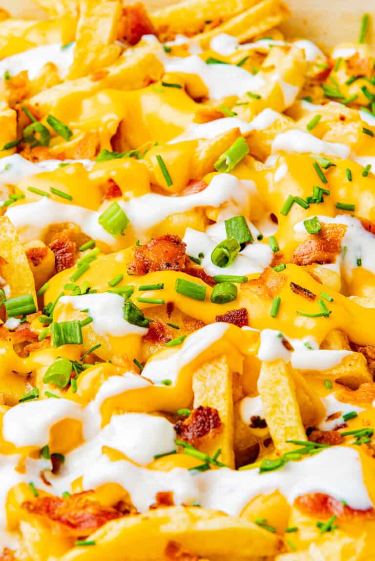 Loaded fries topped with melted cheese, bacon, scallions, and sour cream in a baking dish.