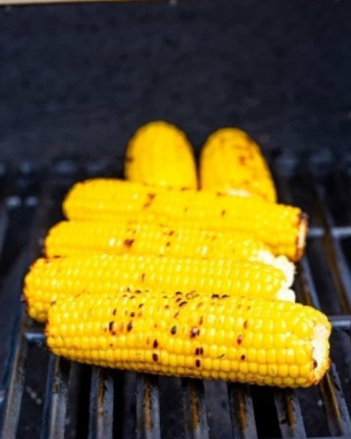 Grilled corn on the cob with char marks sits on a barbecue grill, showcasing a vibrant yellow color and smoky texture.