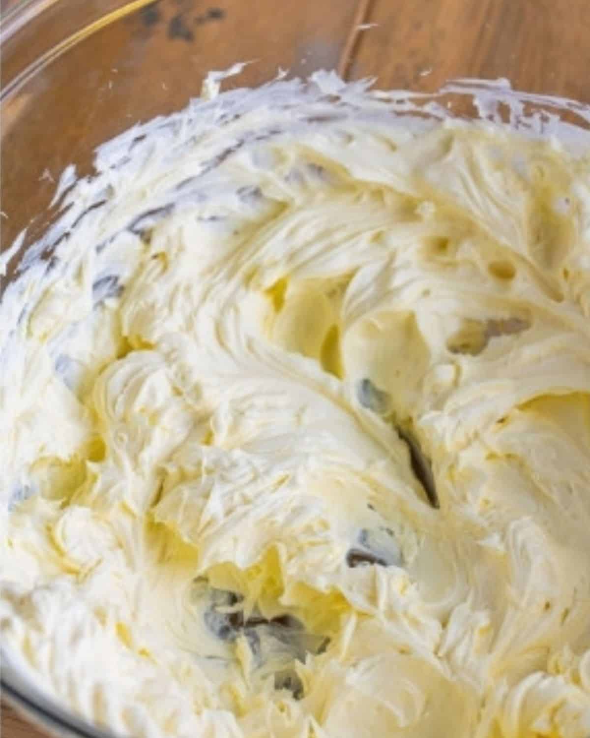 Creamy, smooth cream cheese in a glass bowl on a wooden table.