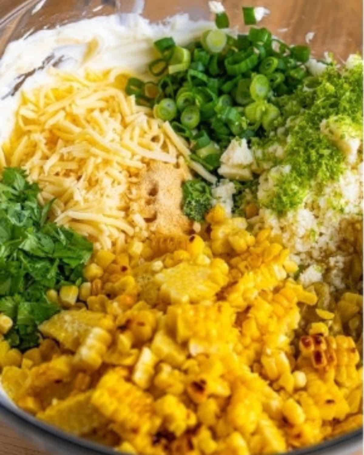 bowl filled with grilled corn, green onions, cilantro, garlic powder and cheese.