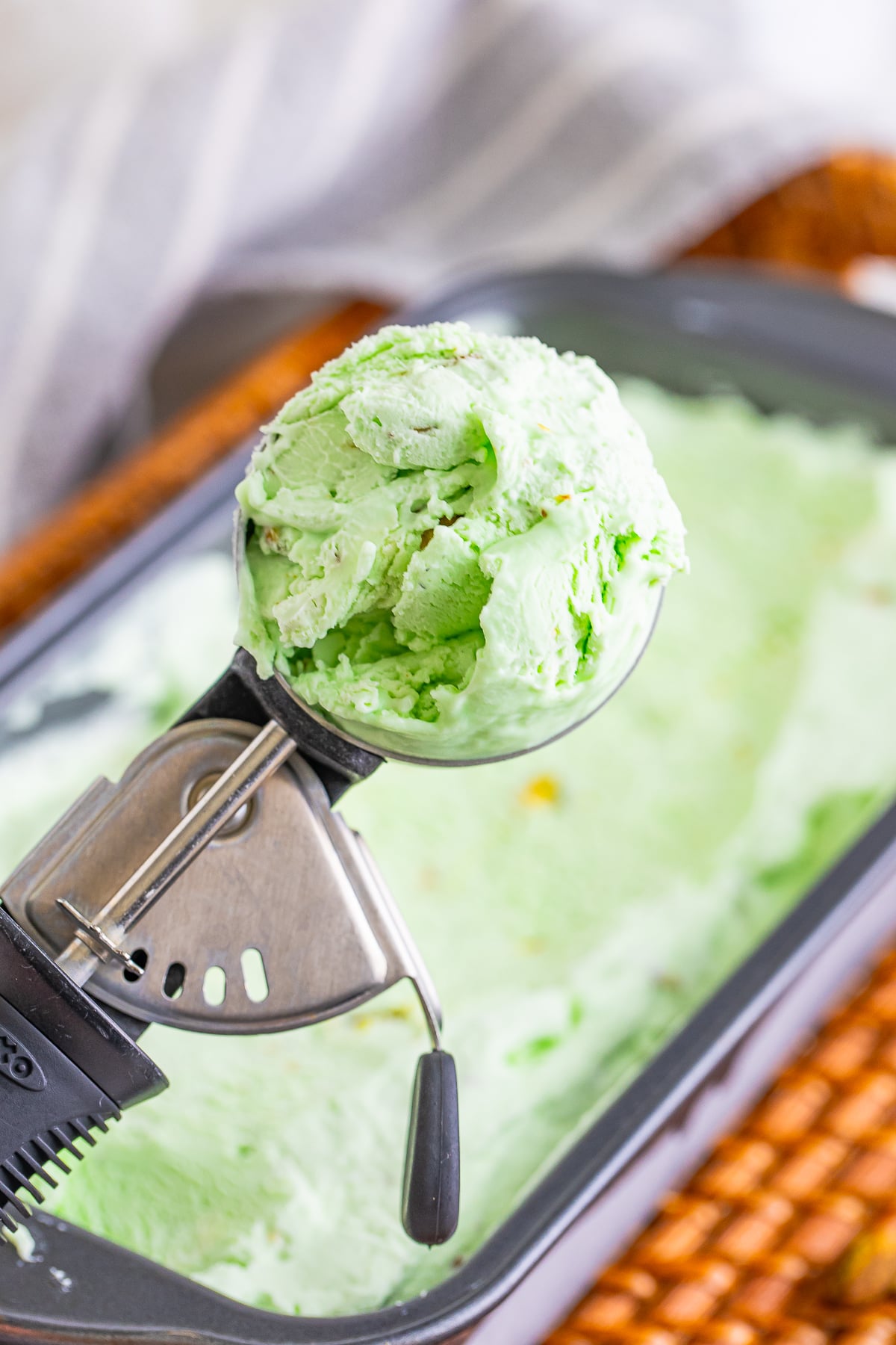 an ice cream scoop holding up a scoop of Pistachio Ice Cream in air