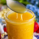 A spoon drizzling thick White Chocolate Sauce back into a glass jar.
