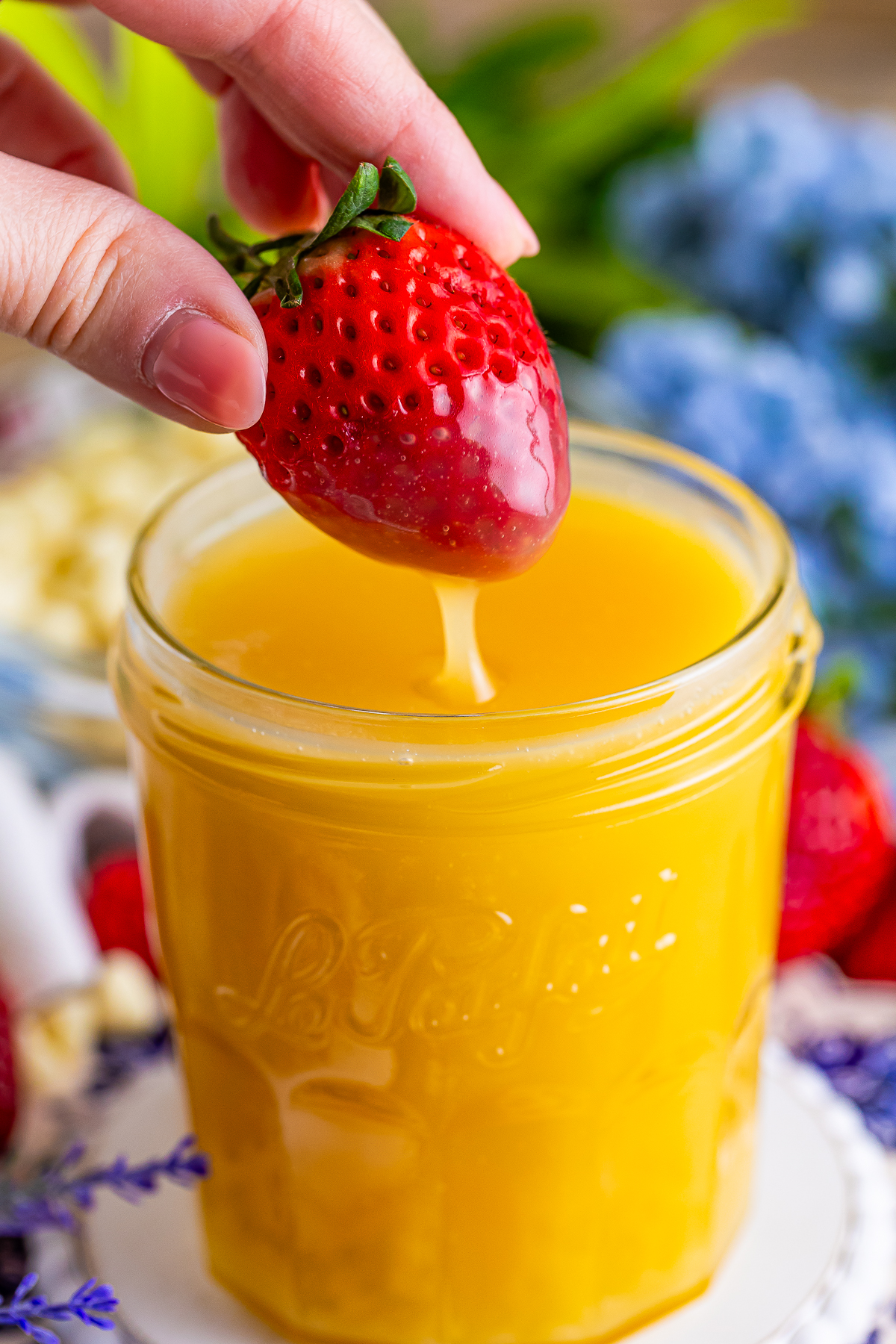 a hand dipping a strawberry into White Chocolate Sauce