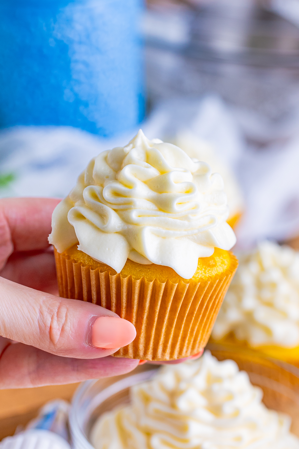a hand holding up a cupcake in the air with Cream Cheese Frosting on top