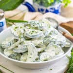 A white bowl of creamy cucumber salad topped with fresh dill and chives.