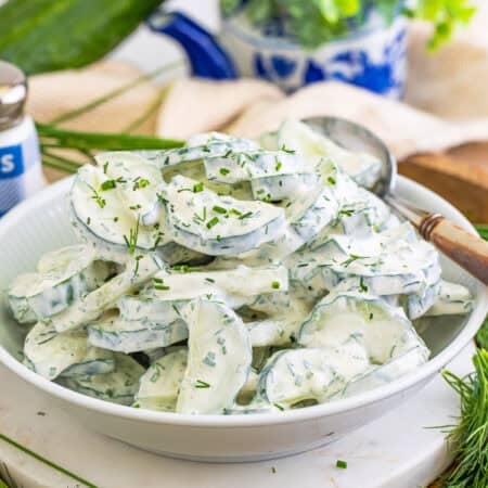 A white bowl of creamy cucumber salad topped with fresh dill and chives.