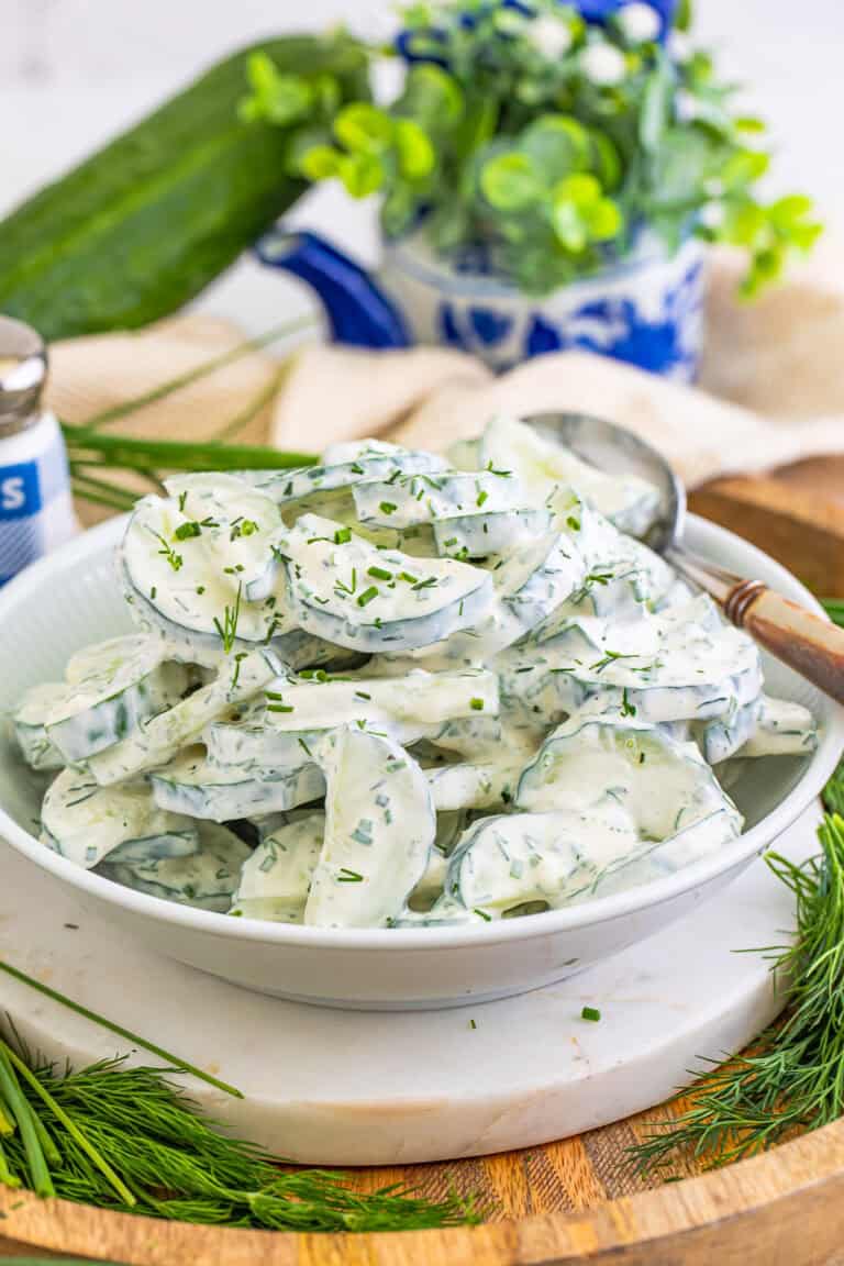 A white bowl of creamy cucumber salad topped with fresh dill and chives.