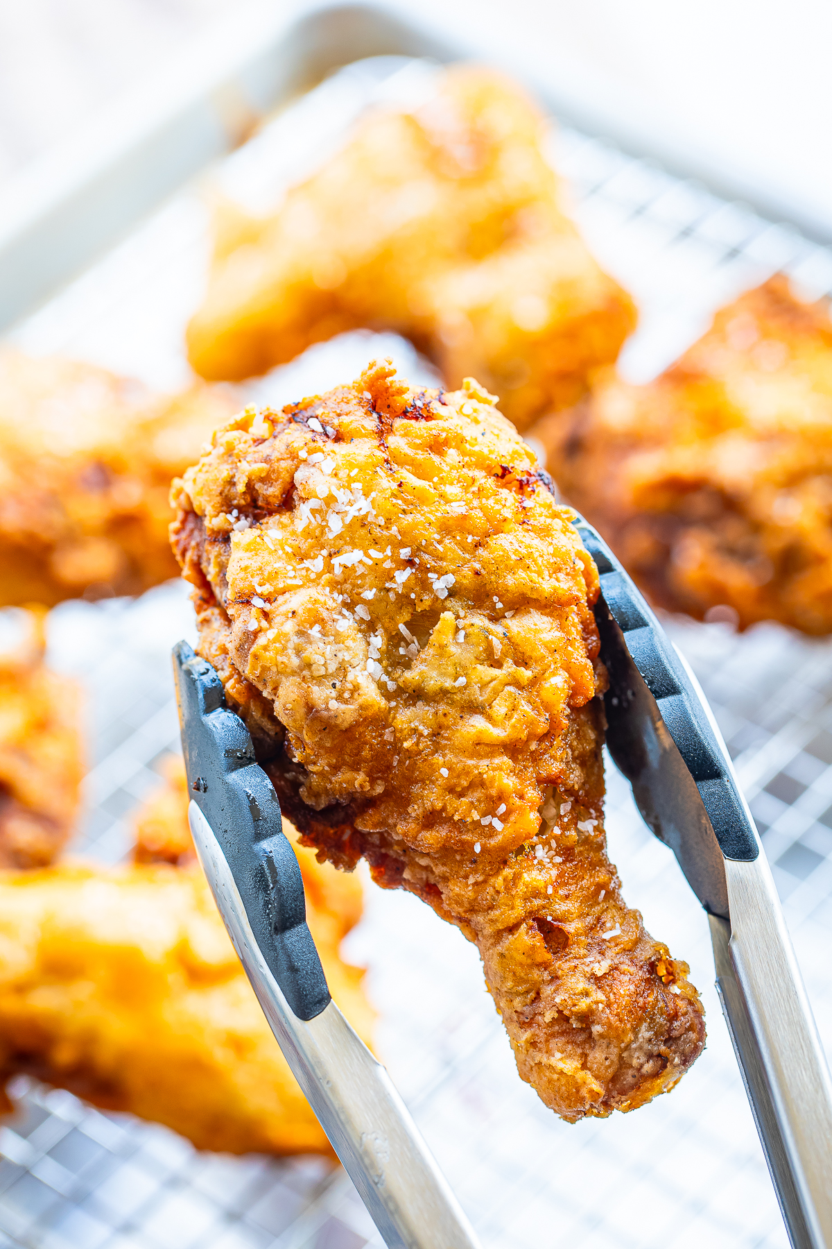 a pair of tongs holding up Louisiana Fried Chicken leg