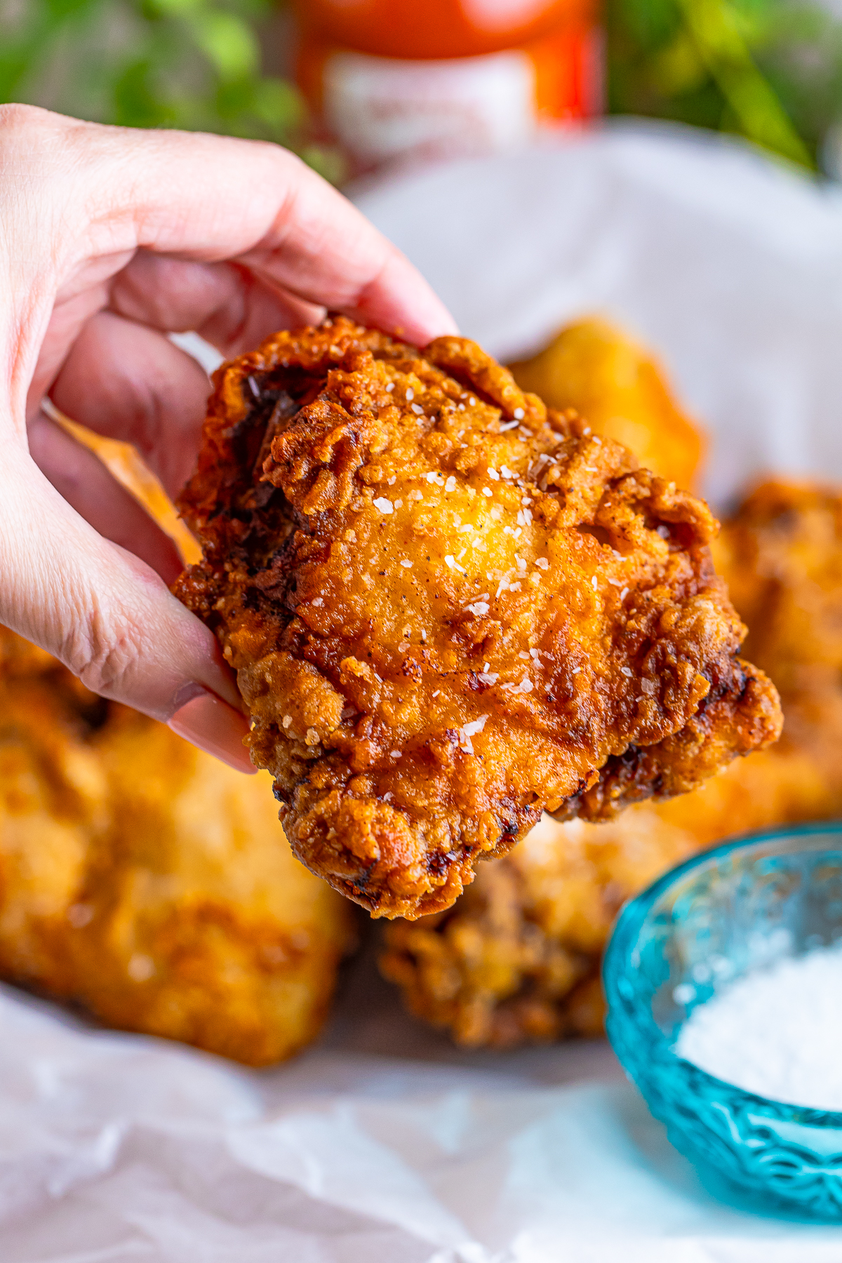 a hand holding up a piece of Louisiana Fried Chicken in air