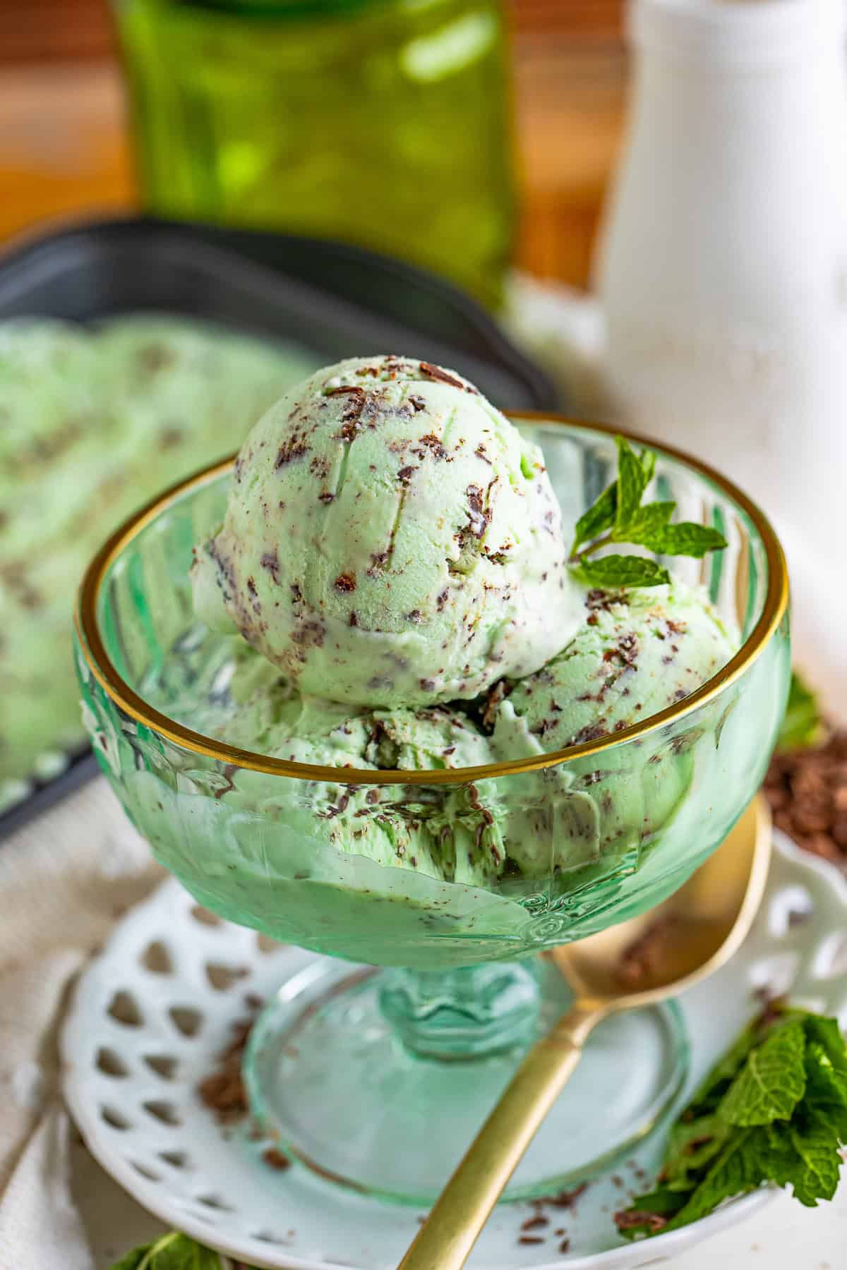 A scoop of mint chocolate chip ice cream in a green glass dish with fresh mint.