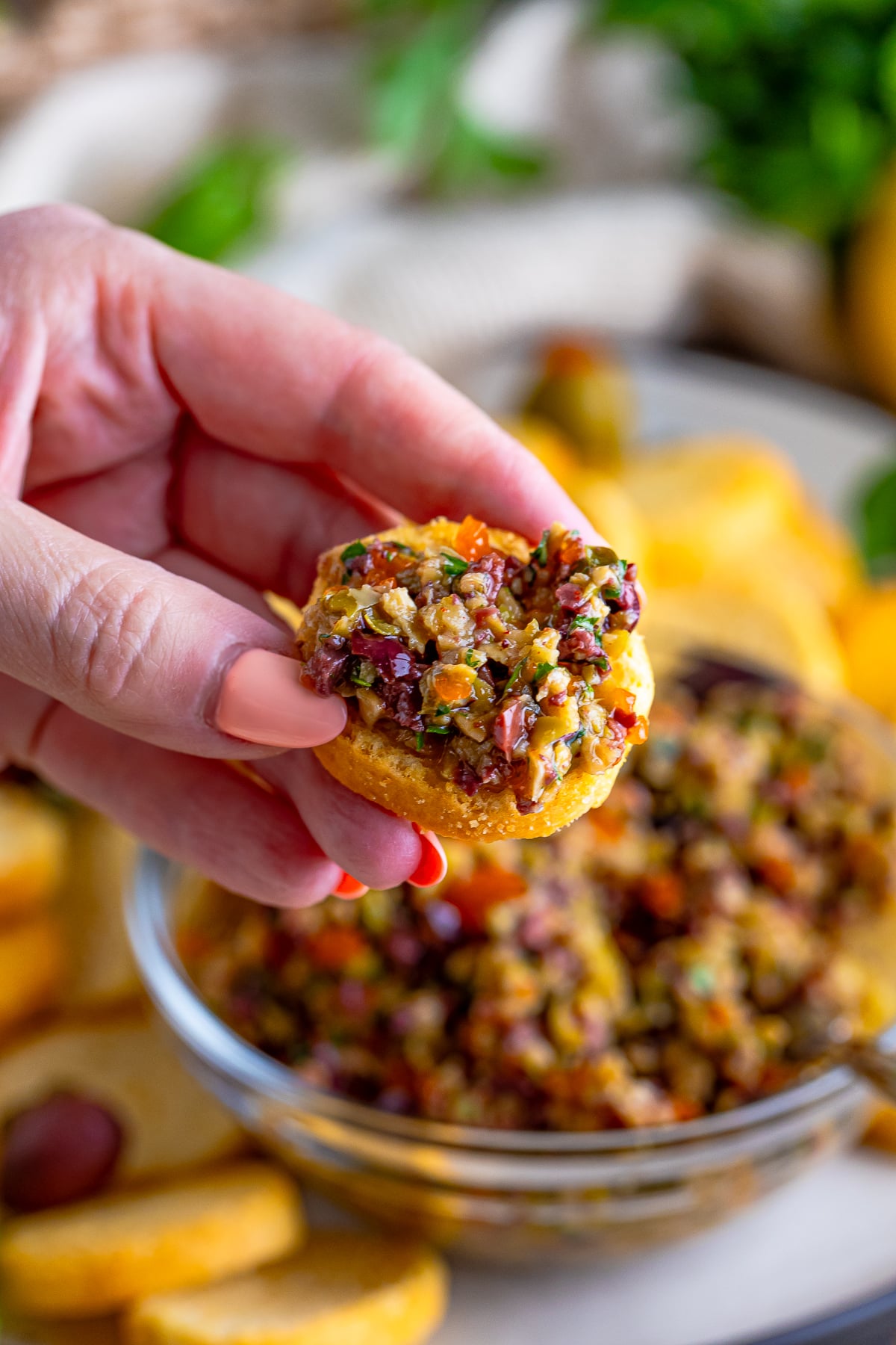 a hand holding up a crostini with olive tapenade on it in air 