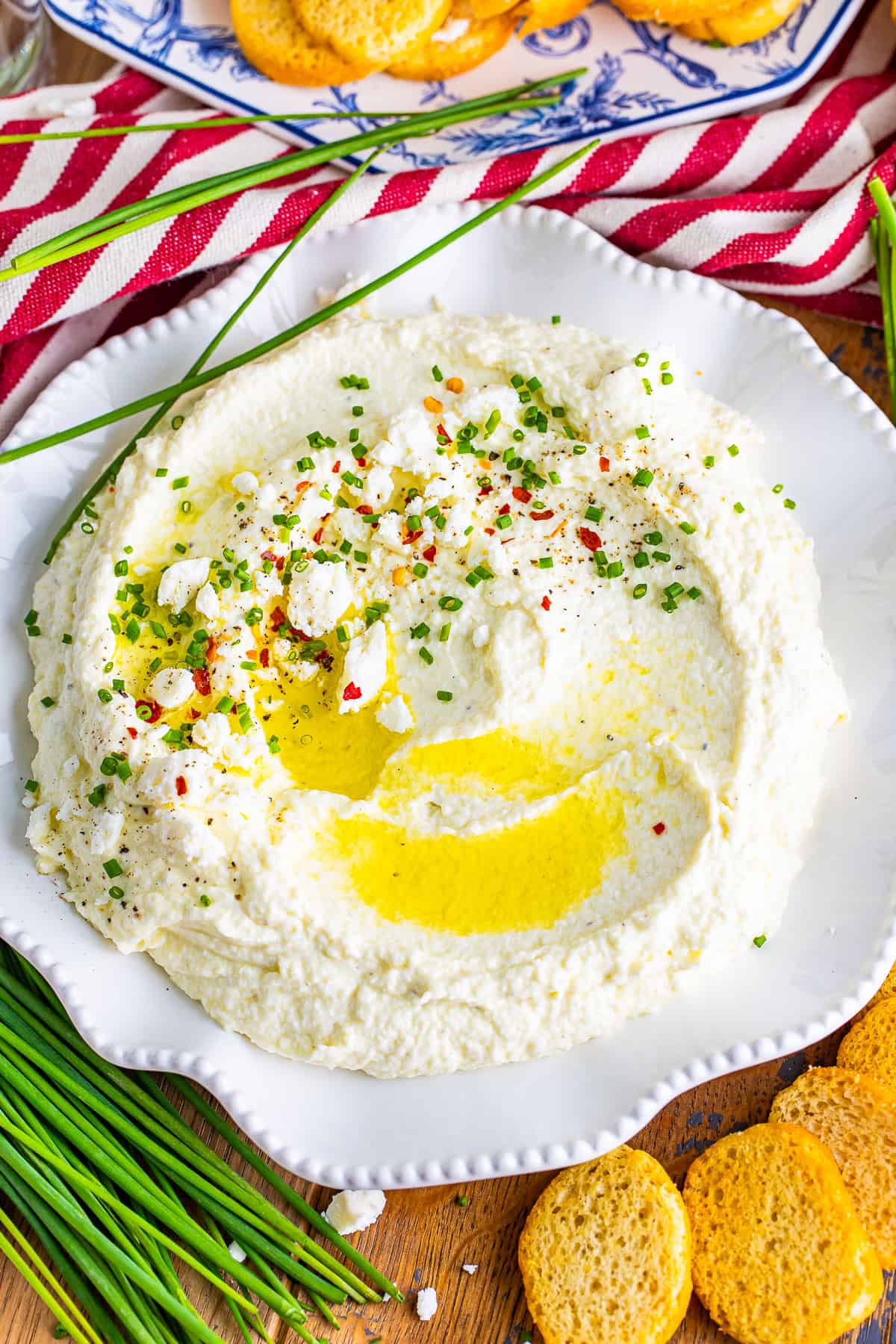 Whipped Feta Dip on a white plate topped with chives, chili flakes, and black pepper.