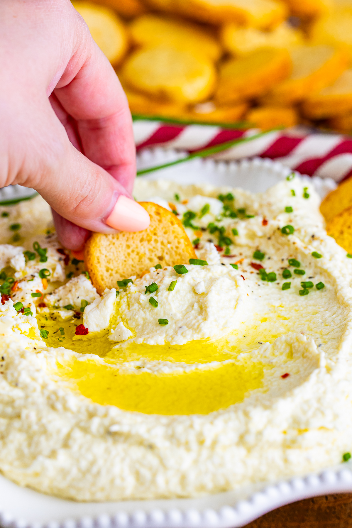 a hand dipping crostini into Whipped Feta Cheese