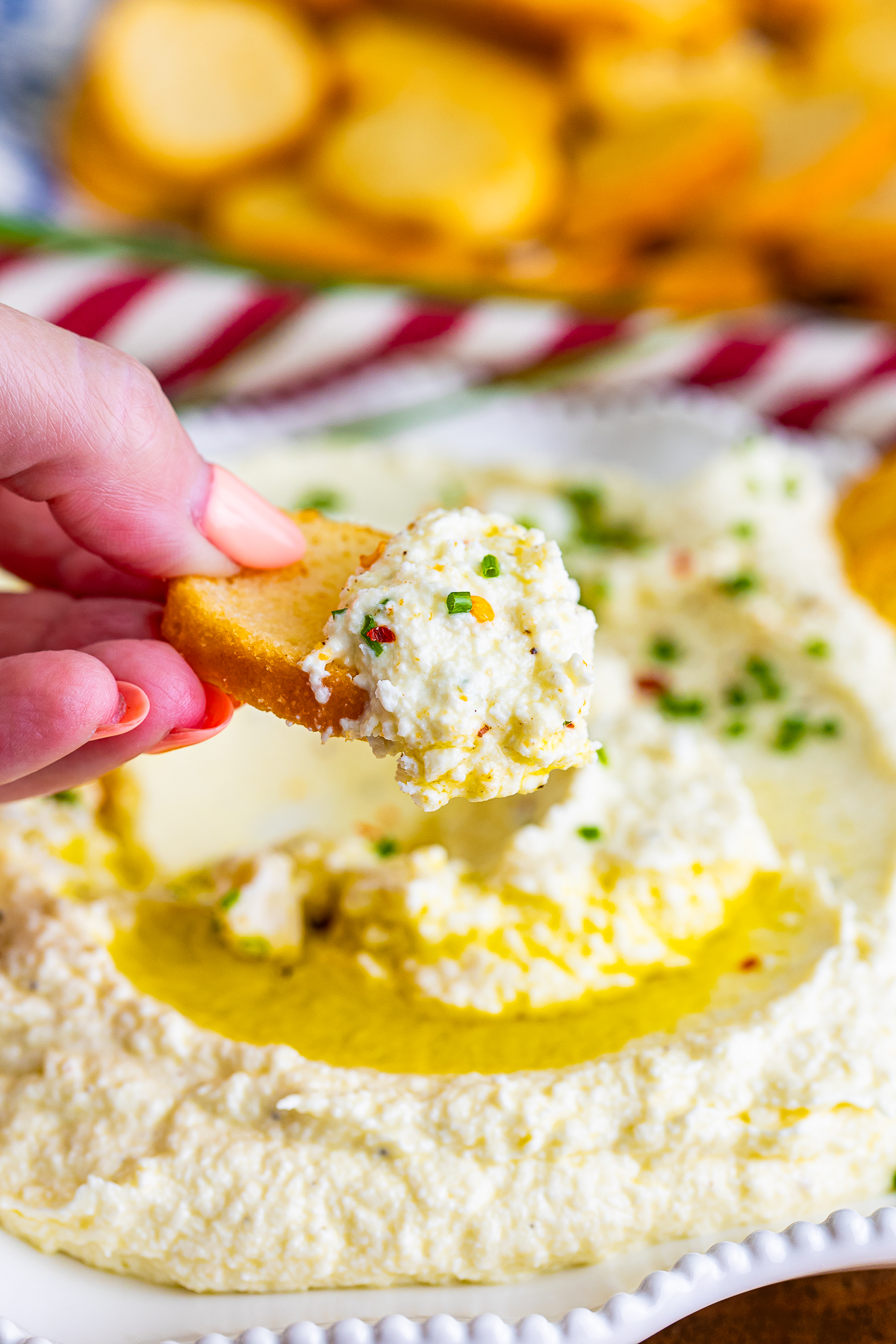a hand holding up a crostini with Whipped Feta Cheese on it in air