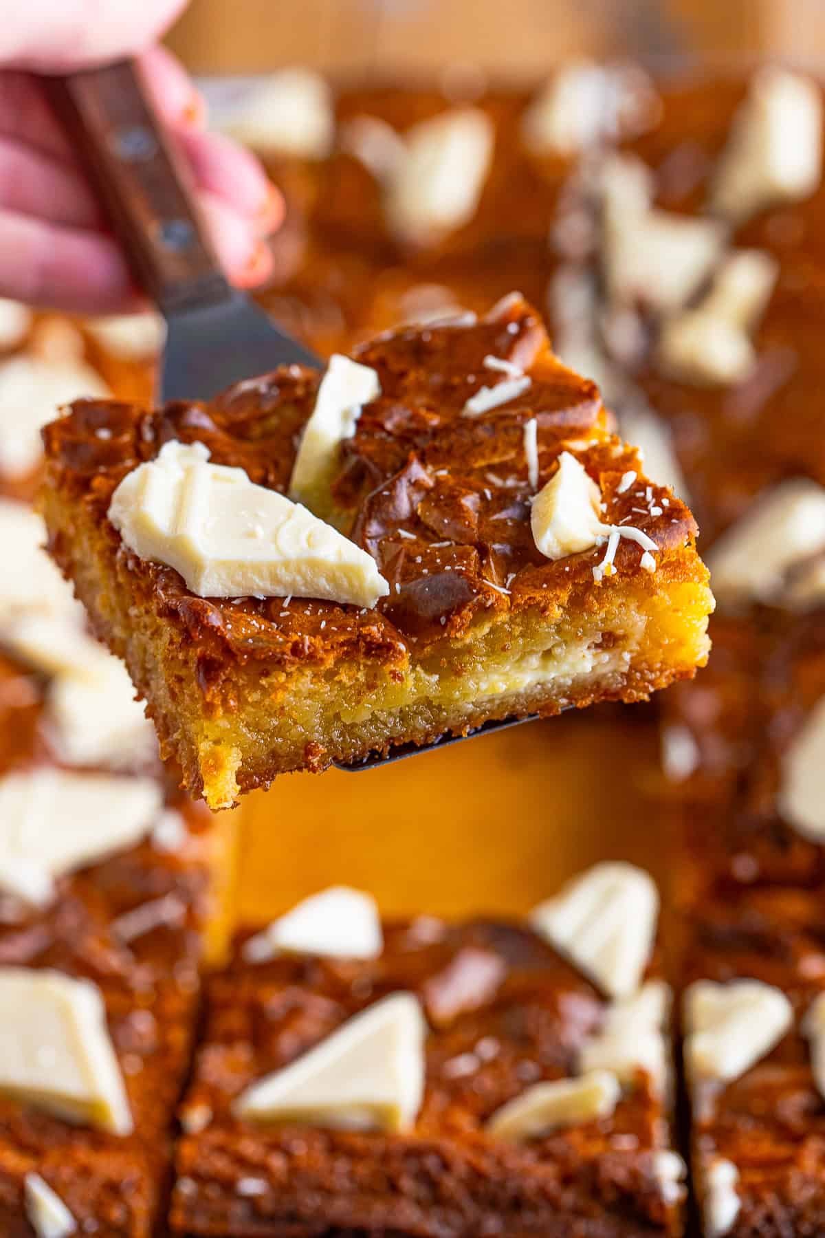 A white chocolate brownie held up to show its dense, gooey, golden center.