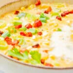 A pot of creamy corn chowder topped with crispy bacon and green onion.