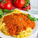 A plate of spaghetti topped with thick Roasted Tomato Sauce, fresh basil, and vine tomatoes in the background.