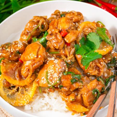 Asian lemon chicken served over white rice in a bowl with chopsticks and fresh cilantro.