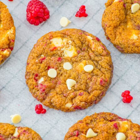 White Chocolate Raspberry Cookies on parchment paper studded with white chocolate chips and fresh raspberry swirls.