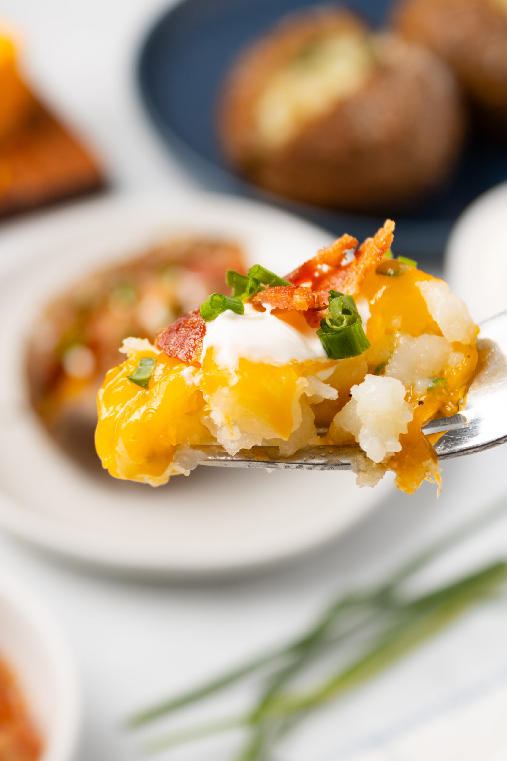 A final picture of a fork full of potato cheddar cheese bacon and chives topped with sour cream.