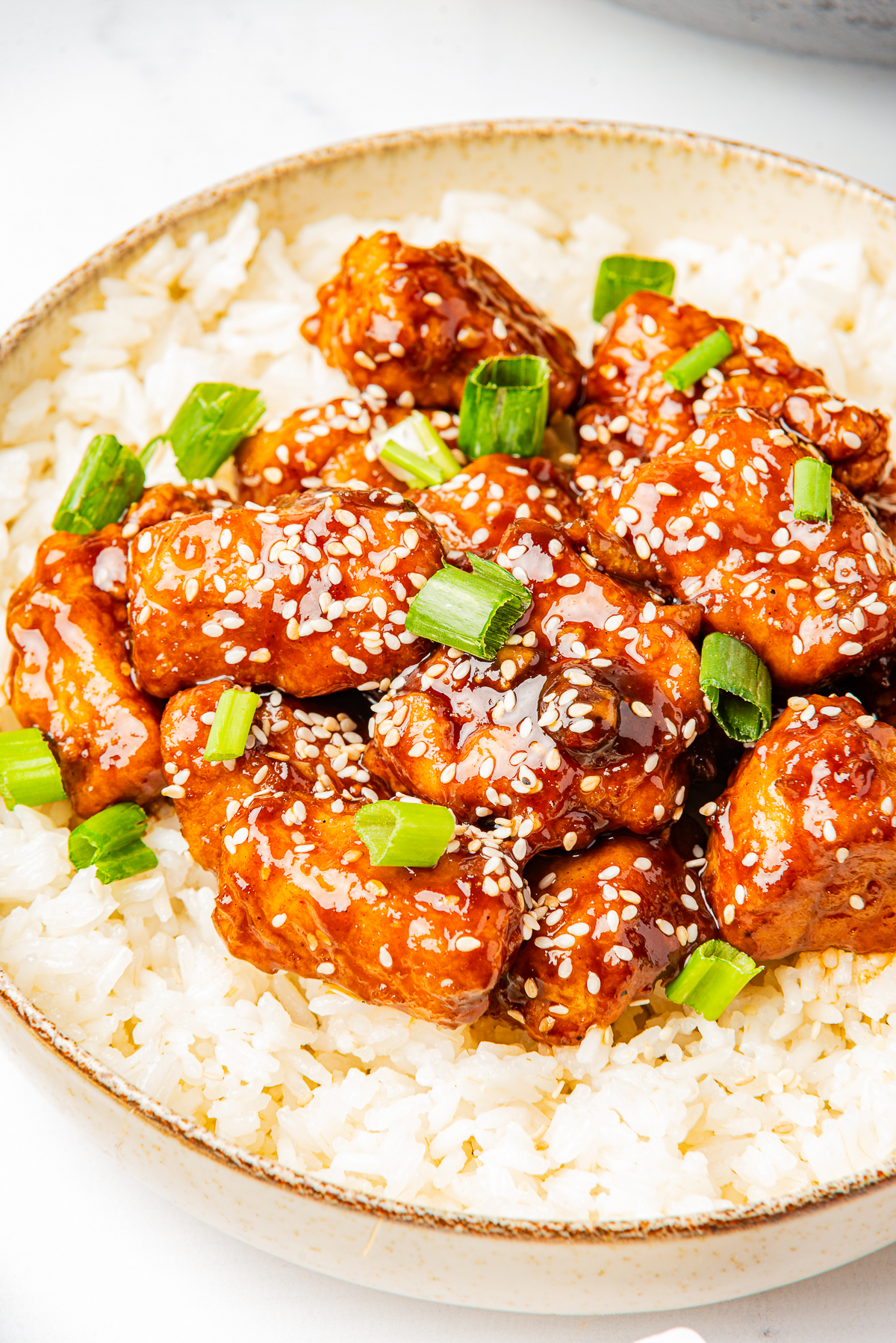 This is a picture of the finished dish.  The chicked is coated a bright orange with sesame seeds and greed onions on the chicken.  It is served on a bed of white rice.