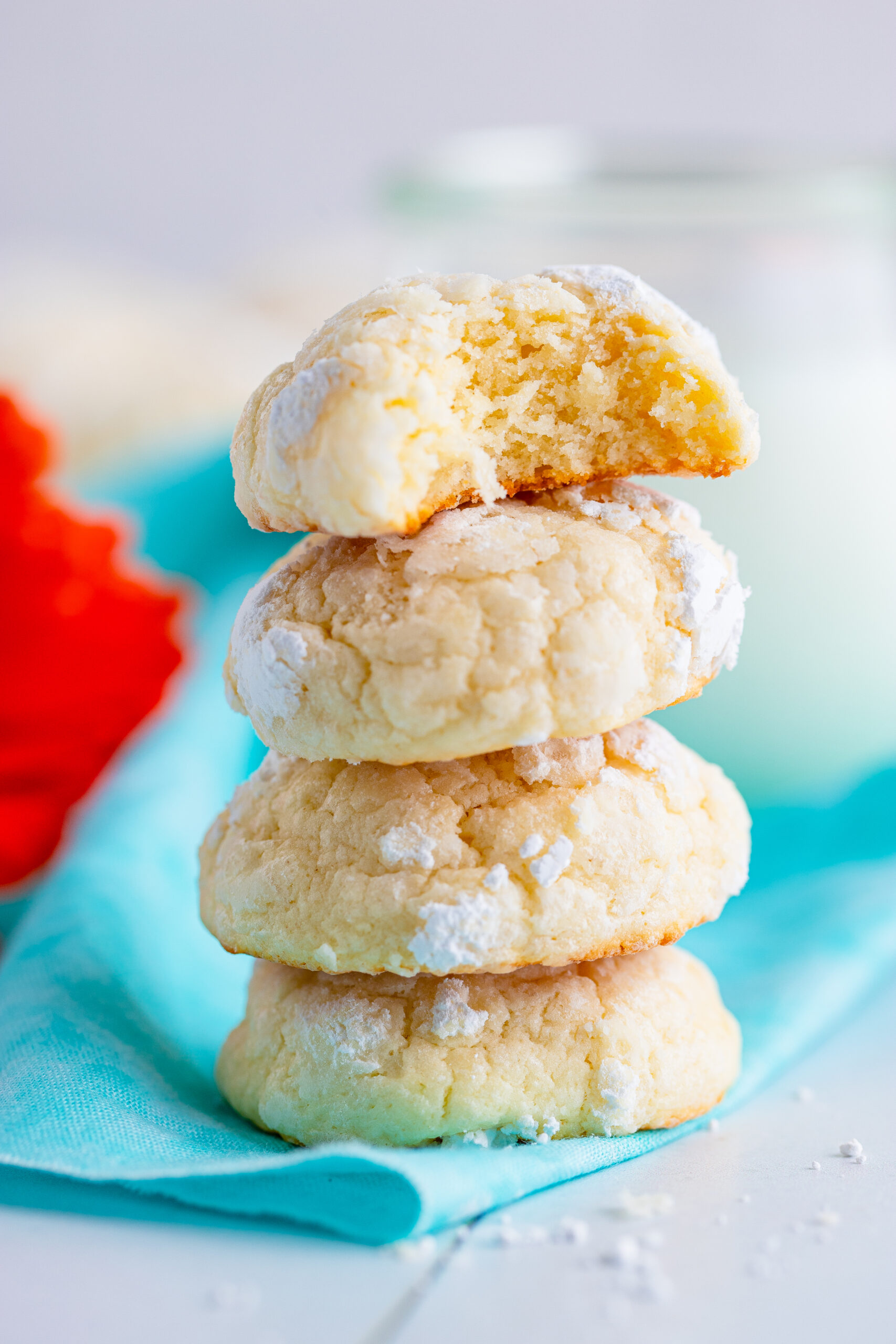 A stack of four cream cheese cookies stacked on top of each other.  There is a orange flower in the back ground.  There is a blue scarf in the ack ground.
