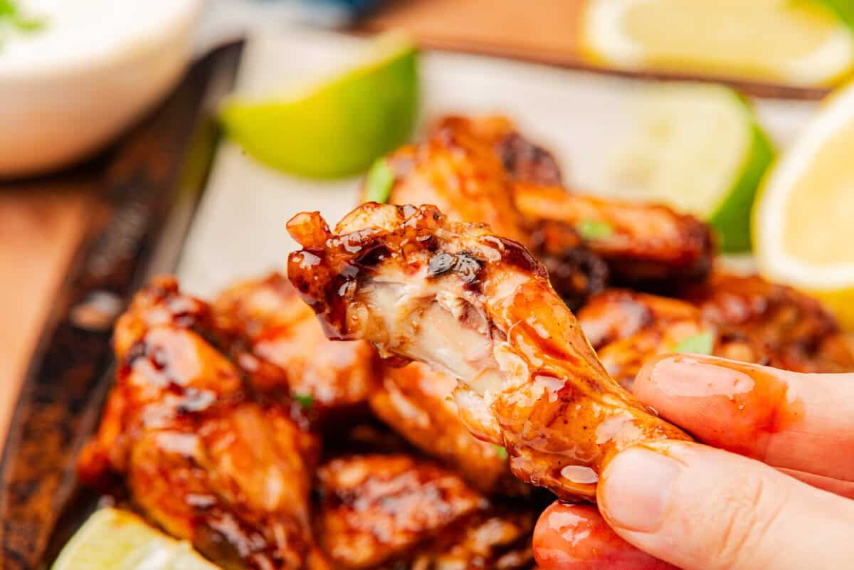 A crispy air fryer chicken wing held up close showing the sticky honey sriracha glaze.