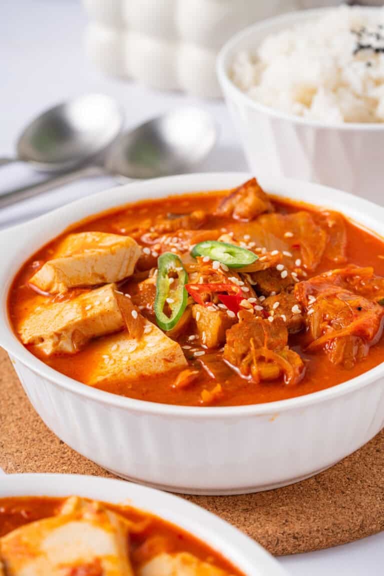 A bowl of spicy red kimchi jjigae with pork belly and tofu served with a bowl of white rice