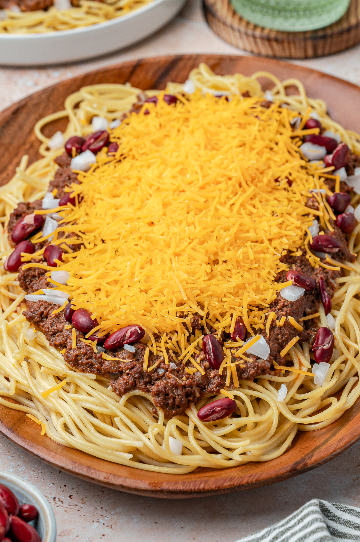 A finished recipe picture of spaghetti topped with the chili plus red beans and cheddar cheese.