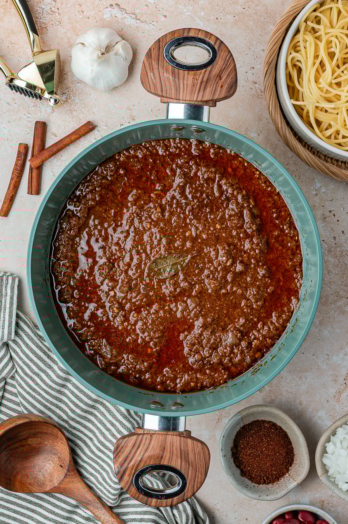 This is a picture of the finished chili with a plate of spagetti, garlic clove, cinnamon, onions and chili powder.