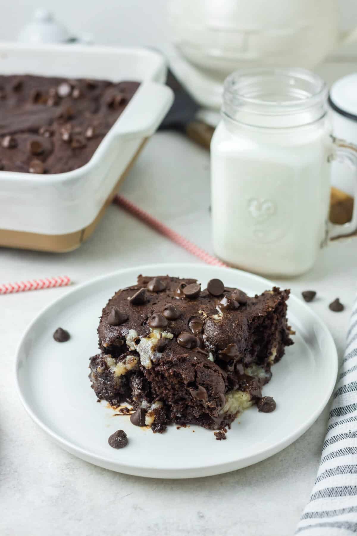 This is a picture of the cake with a bite taken out of it. There in a glass of milk in the background and the rest of the cake in the background