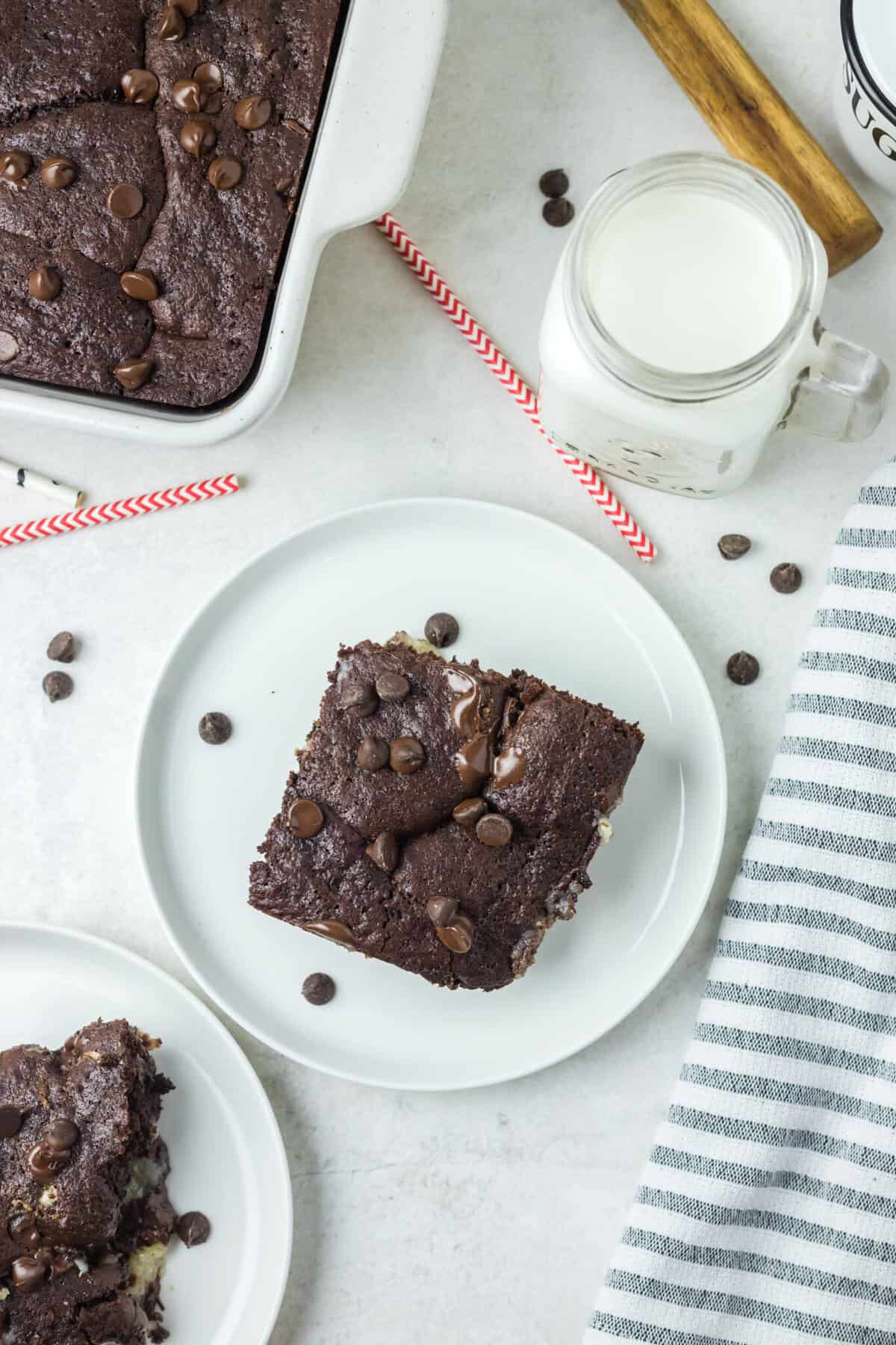 This is a pitcture of a piece of the chocolate earthquake cake with sprinkles of chocolate chips a glass of milk and the remainder of the cake.
