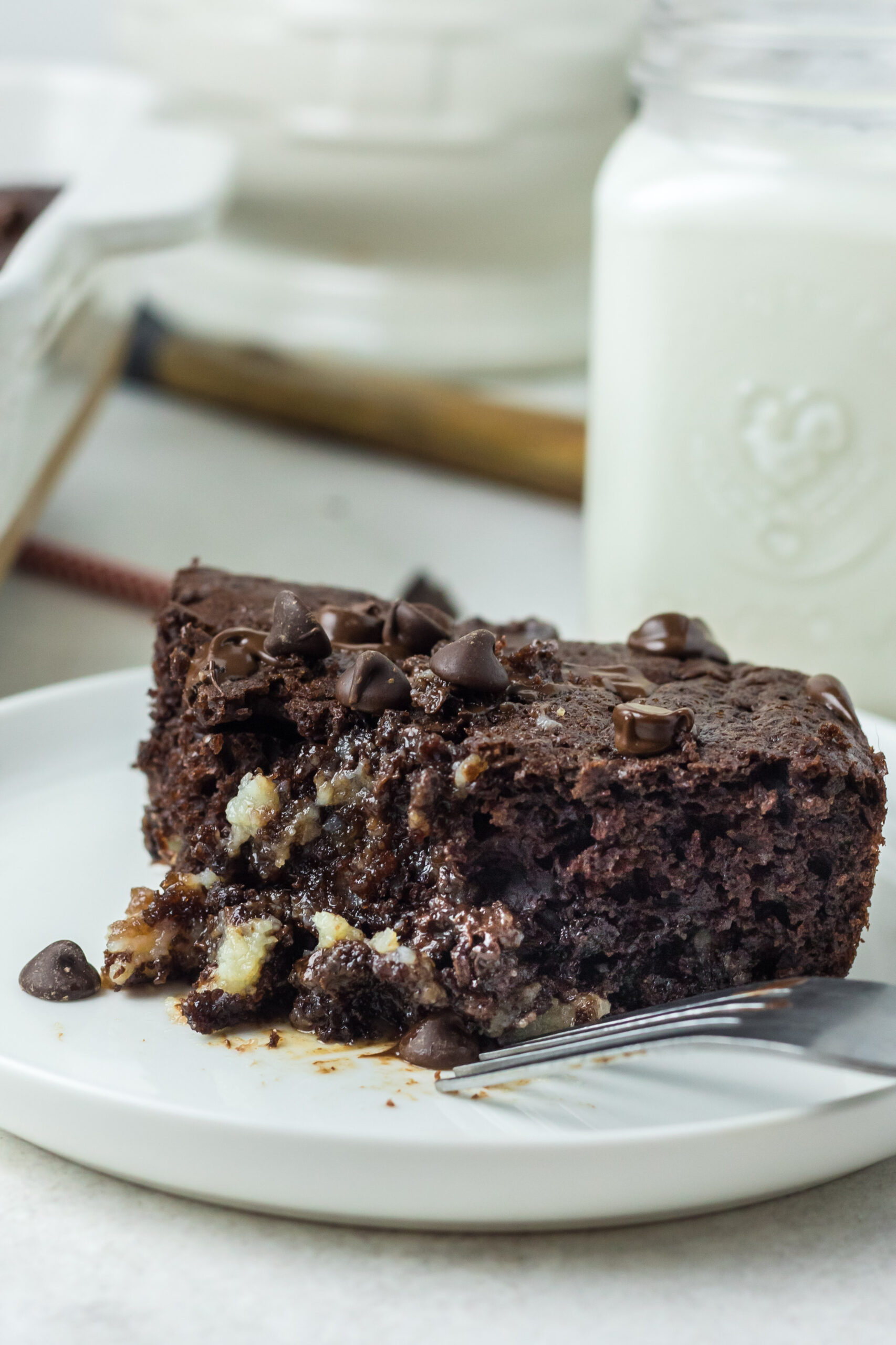This is a picture of the cake with a bite taken out of it.  There in a glass of milk in the background and the rest of the cake in the background