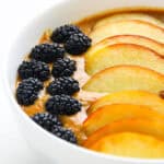 A thick apricot smoothie bowl topped with peach slices, blackberries, and granola.